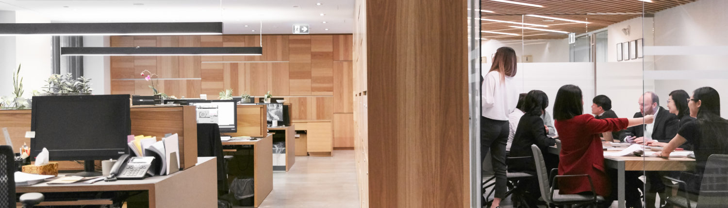 Holborn Group Career Page Interior office with open concept modern desks on the left and a boardroom with a meeting underway on the right